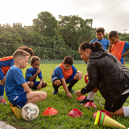 A sports coach guiding young football players during outdoor training